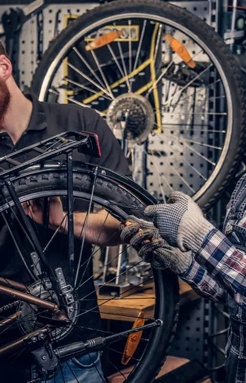 Werkstatt für Fahrrad und E-Bike, Mechaniker mit Handschuhen am ausgebauten Hinterrad