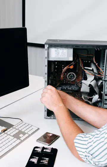 Computerwerkstatt, Hand im geöffneten Tower-PC neben Monitor und Tastatur