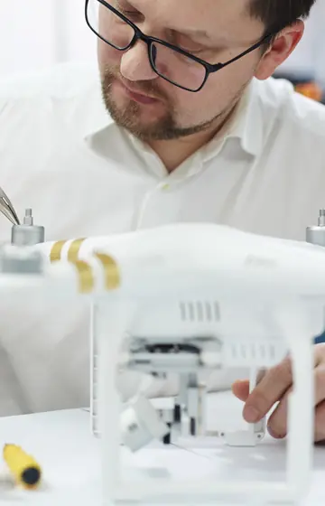 Drohnenwerkstatt, Techniker mit Brille prüft eine weiße Drohne auf dem Tisch