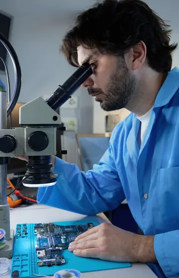 Bauteilreparatur, Techniker im blauen Kittel am Mikroskop über einer Platine