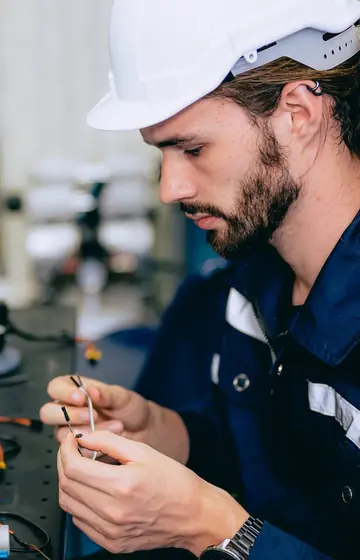 Industrieelektronik, Techniker mit Schutzhelm verkabelt ein Bauteil an der Anlage