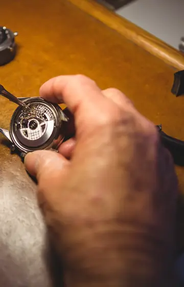 Uhrmacher hält ein offenes Uhrwerk mit dem Schraubendreher in der Hand